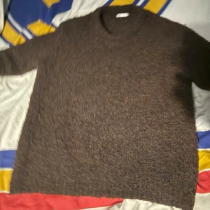 Brun stickad tröja med rund hals - Mysig brun stickad tröja med rund hals och långa ärmar. Perfekt för kyliga dagar och enkel att matcha med jeans eller andra favoritplagg. Tröjan har en loose passform och är tillverkad i ett mjukt material som känns skönt mot huden.