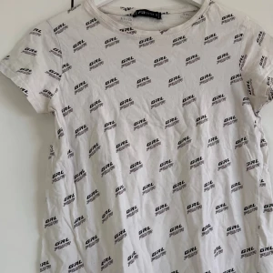 Vit t-shirt med tryck från NEW YORKER  - Vit t-shirt från NEW Yorker  med coolt all-over tryck 'GRL PWR' i svart. Modellen har rund hals och korta ärmar, perfekt för dig som gillar statement-plagg. Materialet är mjuk bomull som känns skönt mot huden. Enkel och snygg passform som funkar till jeans eller shorts.