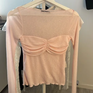 Ljusrosa topp från Gina Tricot - Supersöt ljusrosa mesh topp från Gina Tricot med långa ärmar och rynkad detalj över bröstet. Toppens material är tunt med vågig kant nertill.💕