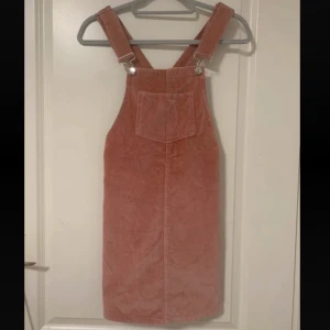 Rosa manchesterklänning med hängslen - Rosa manchesterklänning med breda hängslen och en stor ficka framtill