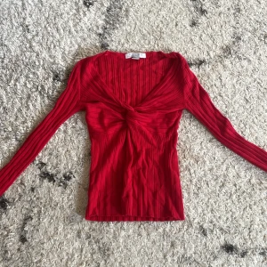 Röd ribbad långärmad topp Amisu XS - Säljer en röd ribbad långärmad topp från Amisu i storlek XS. Toppen har en snygg v-ringning och twistad detalj framtill som ger en cool look. Materialet är stretchigt och sitter figurnära. Perfekt för dig som gillar färg och vill sticka ut.