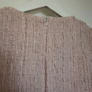 Ljusrosa kort klänning med pärlknappar - Supersöt ljusrosa kort klänning i strukturerat tyg med v-ringning och pärlknappar framtill. Klänningen har korta ärmar, dekorativa fickor med pärldetaljer och dragkedja i ryggen. Perfekt för dig som gillar en chic och feminin stil. Vet ej märke men passar S / M