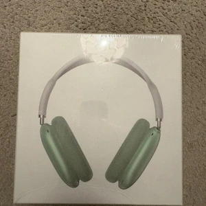 AirPods Max - Apple AirPods Max i grönt, trådlösa over-ear hörlurar med aktiv brusreducering och hög ljudkvalitet. Produkten är i originalförpackning och ser ut att vara i nyskick, perfekt för musikälskare som söker premiumljud och komfort.