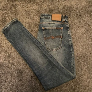 Blå jeans från Nudie Jeans - Snygga blå jeans från Nudie Jeans med klassisk orange söm och broderad detalj på bakfickorna. Modellen är ”skinny lin”. Hör av er vid frågor eller funderingar 