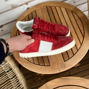 Flycrews  - Säljer ett par röda Valentino Garavani sneakers i mocka med vit detalj på sidan och vit sula. Skorna har snörning och coola nitar bak på sulan. Insidan är vit och sulan har ett unikt mönster. Perfekta för dig som vill sticka ut med lyxiga och snygga sneakers.