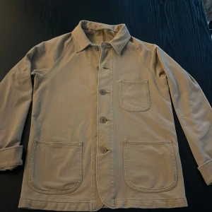 Beige overshirt med stora fickor - Snygg beige overshirt med klassisk krage och tre stora framfickor. Jackan har knäppning med knappar och raka, långa ärmar. Perfekt för lager-på-lager och enkel att matcha med jeans eller chinos. Stilren och minimalistisk design.