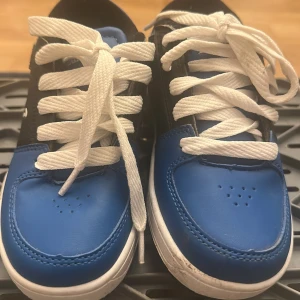 Sidewalk Sports blå svarta sneakers med hjul - Säljer ett par blå och svarta sneakers från Sidewalk Sports med vita snören och inbyggda hjul i sulan. Skorna har rund tå, perforerade detaljer framtill och cool logga på sidan och sulan. Perfekta för dig som vill rulla fram med stil!