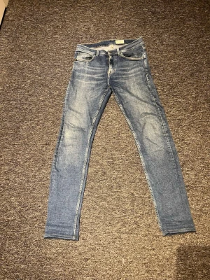 Tiger of Sweden Leon jeans blå 29/32 - Snygga blå jeans från Tiger of Sweden i modellen Leon. De har en klassisk femficksdesign, slim fit och är tillverkade i jeansmaterial med ljusa slitningar. Passar dig som gillar smalare siluett och stilren look.