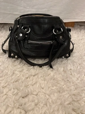 Svart handväska med silverdetaljer - Snygg svart handväska i skinnimitation med silverfärgade nitar och dragkedjor. Det får plats med nästan vad som helst, säljer då den inte kommer till användning längre 