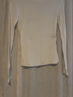 Vit ribbad långärmad topp - Säljer en vit långärmad topp med ribbad struktur och slits i nederkanten. Toppen har en enkel och stilren design med rund hals och är tillverkad i mjukt material som sitter bekvämt mot kroppen. Perfekt att matcha med jeans eller kjol.