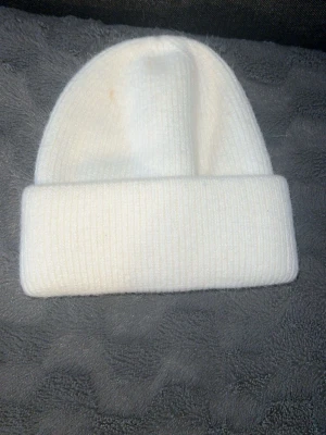 Ingen väst på bilderna - Bilderna visar en vit ribbstickad mössa, inte en väst. Kan ej ge detaljerad beskrivning eller taxonomier för väst då ingen sådan syns.