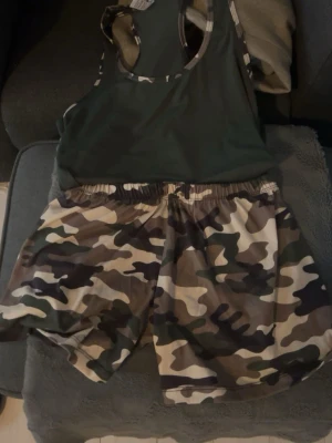 Kamouflage pyjamas  - Säljer ett par snygga pyjamas med klassiskt kamouflagemönster i gröna, bruna och beige toner. Shortsen har elastisk midja och är gjorda i lätt syntetmaterial som andas bra.