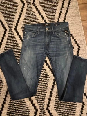 Replay 29/32 - Säljer ett par Replay Jondrill jeans i blå tvätt med snygga slitningar i storlek W29/L32. 