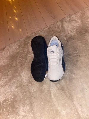 Vita sneakers från Denim ASR - Säljer ett par fräscha vita sneakers från Denim ASR med svarta och guldiga detaljer på sidorna. Skorna har rund tå, platt sula och snörning framtill. Materialet är syntet och textil, med en mjuk och vadderad insida för extra komfort. Perfekt för dig som gillar stilrena och sportiga skor.