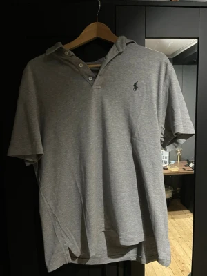 Grå Polo Ralph Lauren t-shirt - Snygg grå t-shirt från Polo Ralph Lauren i klassisk modell med korta ärmar och krage. T-shirten har knappar vid halsen och den ikoniska broderade loggan på bröstet. Tillverkad i mjuk bomull som är skön mot huden. Perfekt för en chill och stilren look.