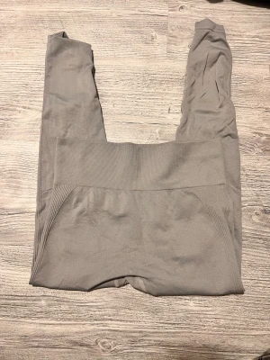 Grå höga leggings med ribbad midja - Snygga grå leggings med hög ribbad midja som sitter skönt och ger extra stöd. Materialet är stretchigt och mjukt, perfekt för träning eller chill. Diskret design utan synliga loggor och med sömmar som formar och framhäver siluetten.