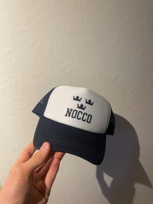 Nocco keps 🧢  - Bilderna visar en blå och vit keps från NOCCO med tre kronor på framsidan, inte använd helt ny limeterad 