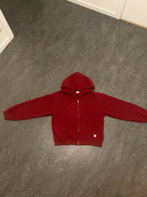 Akimbo Club Zip Up Hoodie “Strawberry Red” - Säljer en Akimbo Club Zip Up Hoodie “Strawberry Red”, storlek M men passar som S. En baggy men lite cropped proportionalitet. För ytterligare detaljer kom PM