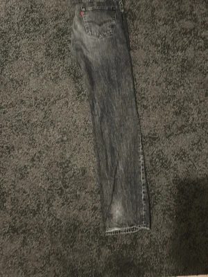 Levi's 501 svarta jeans W32 L34 - Säljer ett par klassiska Levi's 501 jeans i svart tvättad denim. Modellen har rak passform och fem fickor, med den ikoniska läderpatchen bak i midjan. Perfekt för dig som gillar tidlös stil och vill ha jeans med lite edge.