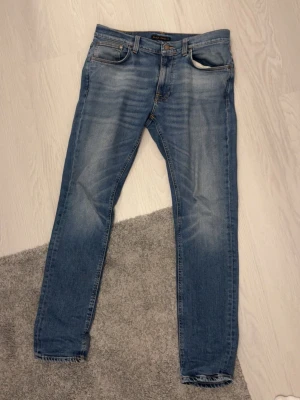 Blå lean dean Nudie Jeans - Säljer ett par blå lean dean jeans från Nudie Jeans. Jeansen har en ljus tvätt, samt Nudie Jeans logga på bakfickan och läderpatch i midjan. Storlek 32x32