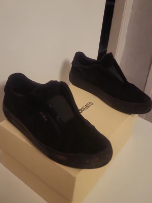 Arigatos (Buda) - Lite jord på som jag inte orkat fixa annars bra skick. Säljer ett par helsvarta sneakers med platt sula och rund tå. Skorna har klassisk snörning och är tillverkade i ett syntetmaterial med tygdetaljer. Perfekta för dig som gillar en clean och enkel stil. Box kommer med