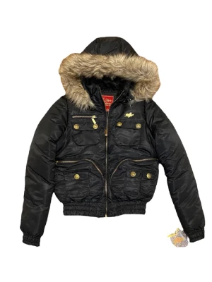 Apple Bottoms jacka - Svart pufferjacka med huva och beige päls från Apple Bottoms. Jackan har guldfärgade knappar, dragkedjor och broderad logga på ryggen. Flera fickor framtill och elastisk midja ger en snygg och bekväm passform. Perfekt för kalla dagar.