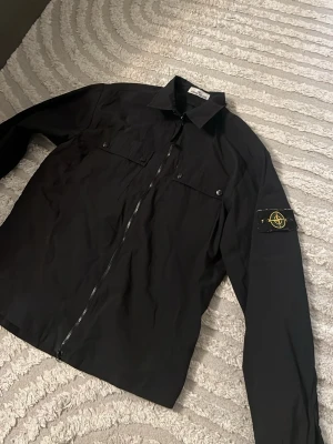 Svart jacka från Stone Island - Säljer en svart jacka från Stone Island med klassisk patch på ärmen. Jackan kommer i bra skick och i strl L! Hör av er om frågor!🤩