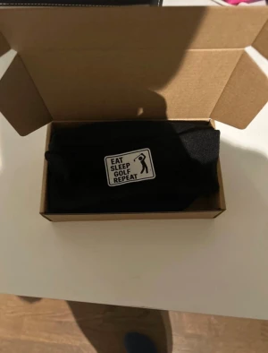 Svart mössa med golf-tryck - Vår varma och goa golfmössa – för riktiga golfälskare Håll värmen på kyliga rundor och visa din passion för spelet med vår sköna golfmössa. Tillverkad i ett mjukt och värmande material som sitter bekvämt hela dagen, både på och utanför banan. Mössan pryds av den populära texten “Eat Sleep Golf Repeat” – ett självklart motto för alla som lever och andas golf. Perfekt för tidiga morgonrundor, sena höstdagar eller bara som en snygg vardagsaccessoar. En given favorit i golfbagen! ⛳️  