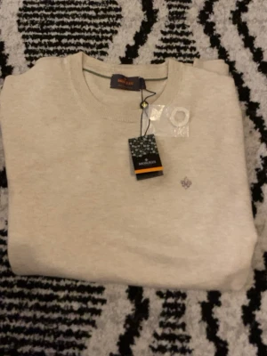 Beige bomullströja från Morris - Snygg beige tröja från Morris i 100% bomull, storlek L. Rund hals och diskret Morris-logga broderad på bröstet. Perfekt för dig som gillar stilrena och klassiska plagg. Tröjan har ribbade muddar vid hals, ärmslut och nederkant. Nypris 1399kr hör av er vid funderingar eller prisförslag!