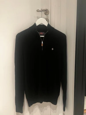 Svart  half zip från Morris - Svart långärmad tröja från Morris i 100% merinoull med half zip och snyggt broderad logga på bröstet. Tröjan har ribbade muddar och en stilren, klassisk look som passar perfekt till höst och vinter. Dragkedjan har en läderdetalj för extra stilpoäng. Storlek L men passar även M.