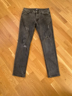 Grå slitna slim-fit jeans - Säljer ett par grå slim-fit jeans med slitningar och trasiga detaljer på både fram- och baksida. Jeansen har klassisk femficksdesign och är tillverkade i ett mjukt jeansmaterial. Perfekta för en avslappnad och trendig look.