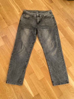 Grå straight jeans med tvättad look - Säljer ett par grå jeans med tvättad vintage-look och raka ben. Klassisk femficksmodell med normal passform och midja. Jeansen är i ett mjukt denimtyg och har snygga slitningar framtill för en avslappnad vibe.