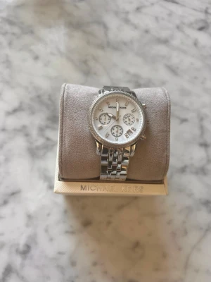 MK klocka  - Bilderna visar en silverfärgad klocka från Michael Kors med länkarmband och glittriga detaljer på urtavlan, men ingen väst finns med.