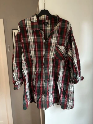 Rutig pyjamas i bomull med knappar - Säljer en rutig pyjamas i mjuk bomull. Pyjamasen har klassiskt röd, grön och vit färgkombination, knappar framtill och en bröstficka. Knappt använd. Skrynklig på bilden. Byxorna är 3/4 långa. 