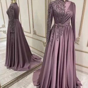 Lila långklänning med spetsdetaljer - Elegant lila långklänning med långärmad design och vackra spetsdetaljer på överdelen. Klänningen har omlott-effekt och ett svepande, utsvängt kjolparti som ger en lyxig känsla. Perfekt för speciella tillfällen och bal.