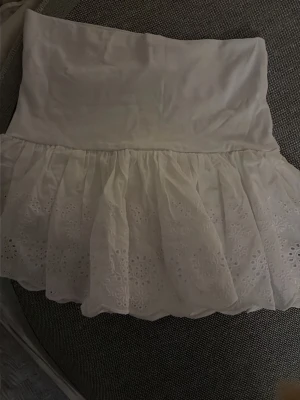 Vit kortkjol med broderade detaljer - Supersöt vit kortkjol med bred midjeresår och volangig nederdel. Kjolen har broderade blommönster. Perfekt till sommaren och lätt att matcha med linnen. I storlek S och från Subdued! Aldrig använd!!