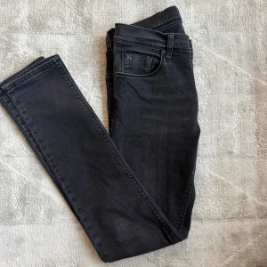 Svarta slim fit jeans från J.Lindeberg - Snygga svarta jeans från J.Lindeberg med klassisk femficksdesign och diskret logga på fickan. Modellen är slim fit och tillverkad i mjukt stretchigt jeansmaterial. Perfekta för dig som gillar stilrena och moderna jeans.