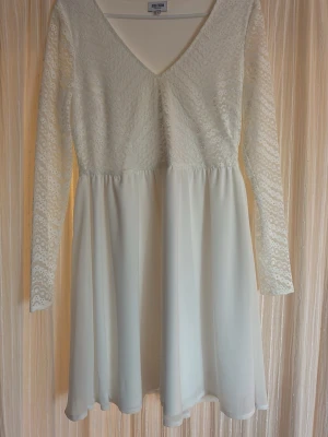 Vit spetsklänning från Bubbleroom - Supersöt vit klänning från Bubbleroom med långärmade spetsdetaljer och v-ringad hals. Överdelen har ett fint spetsmönster och kjolen är slät och lätt utsvängd. Perfekt för dig som gillar romantisk stil och vill ha något ljust och fräscht. säljer pågrund av fel storlek💗