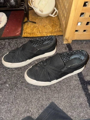 Svarta slip-on sneakers med twist - Säljer ett par svarta slip-on sneakers från Anna Field med snygg twistad detalj över tån 