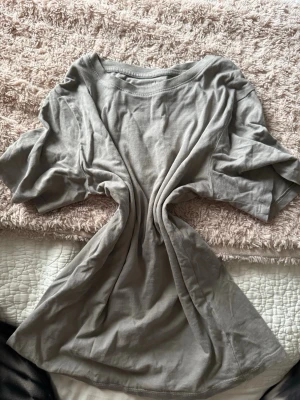 Grå basic t-shirt från H&M - En enkel grå t-shirt från H&M i mjuk bomull. Modellen är klassisk med rund hals och korta ärmar, perfekt för en chill och avslappnad stil. Passar dig som gillar neutrala färger och vill ha en skön t-shirt till vardagen.