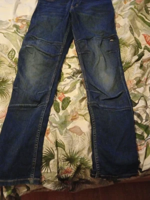 Jeans från Ossoami, storlek 164 - Säljer ett par blå jeans från Ossoami i storlek 164. Jeansen har snygga detaljer på bakfickorna med gul brodering. Klassisk femficksmodell med raka ben och slitningar på framsidan. Perfekt för dig som gillar street och funktion. Pris kan sänkas vid en villig affär.