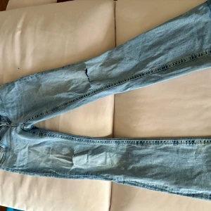 Ljusblå jeans från Gina Tricot, strl 34 - Ljusblå lågmidjade jeans från Gina Tricot med raka ben och klassisk femficksdesign. Snygga detaljer med stora bakfickor med lock och knapp. Jeansen har normal passform och är tillverkade i mjukt denimtyg. Perfekta för en avslappnad stil.
