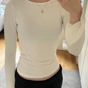 Vit långärmad topp - Säljer en vit långärmad topp. Toppen har en rund halsringning och är tillverkad i ett mjukt, stretchigt material som sitter tight. 