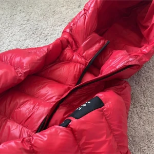 Röd dunjacka från Peak Performance - Säljer en röd dunjacka från Peak Performance med huva och svarta detaljer. Jackan har quiltad design, dragkedja framtill och ribbade muddar. Perfekt för kalla dagar och riktigt snygg färg som sticker ut.