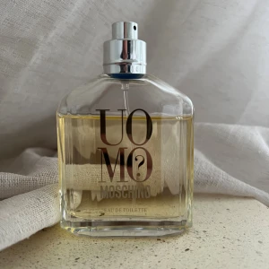 Moschino Uomo EDT  - Moschino Uomo EDT, 75ml (OBS se använd mängd) Doftnot: Kumquat, koriander och brasilianskt rosenträ. Hjärtnoter: Cyklamen, kanel och muskatellsalvia. Basnoter: Cederträ, mysk och ambra. Kork fattas tyvärr. Förvarats mörkt och svalt. 