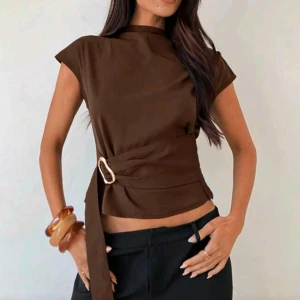Brun omlottopp med bälte - Snygg brun topp med korta ärmar och hög hals. Toppen har ett brett bälte i midjan med metallspänne som ger en omlottkänsla.
