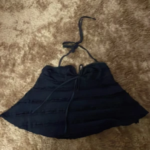 Mörkblå halterneck tubtopp - Säljer en mörkblå tubtopp med halterneck och knytband i nacken. Toppen har en lätt utsvängd form och dekorativa horisontella sömmar som ger en cool struktur. Perfekt för dig som gillar en enkel men ändå trendig look.