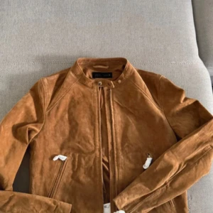 Brun mockajacka från Zara - Snygg brun mockajacka från Zara med minimalistisk design och rund krage. Jackan har dragkedja framtill, långa ärmar och två snedställda fickor. Perfekt för dig som gillar stilrena och trendiga plagg med en lyxig känsla. i storlek S och köpt i vinted!