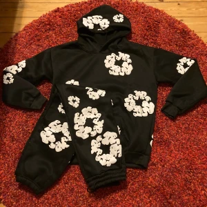 Demin Tears sett  - Svart hoodie med huva och vita grafiska mönster över hela tröjan. Tröjan har långa ärmar, mudd vid ärmslut och nederkant samt en stor ficka framtill. Materialet känns mjukt och passar perfekt för en chill look. 