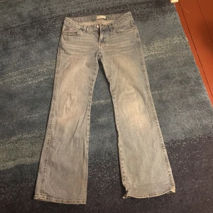 Bootcut jeans i ljus denim, strl 38 - Bootcut jeans i ljusblå denim från Gina. Klassisk femficksmodell med snygga bakfickor med lock och knapp. Jeansen har låg midja och raka ben som går ut i bootcut. Perfekt för dig som gillar retrovibbar och avslappnad stil. Använd fåtal gånger.